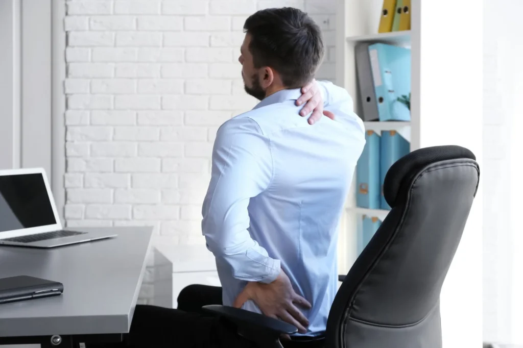 person sitting at desk holding lower back pain office posture