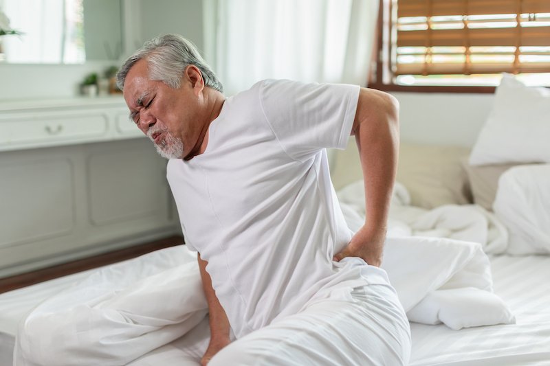person experiencing lower back pain and stiffness while waking up in bed in the morning
